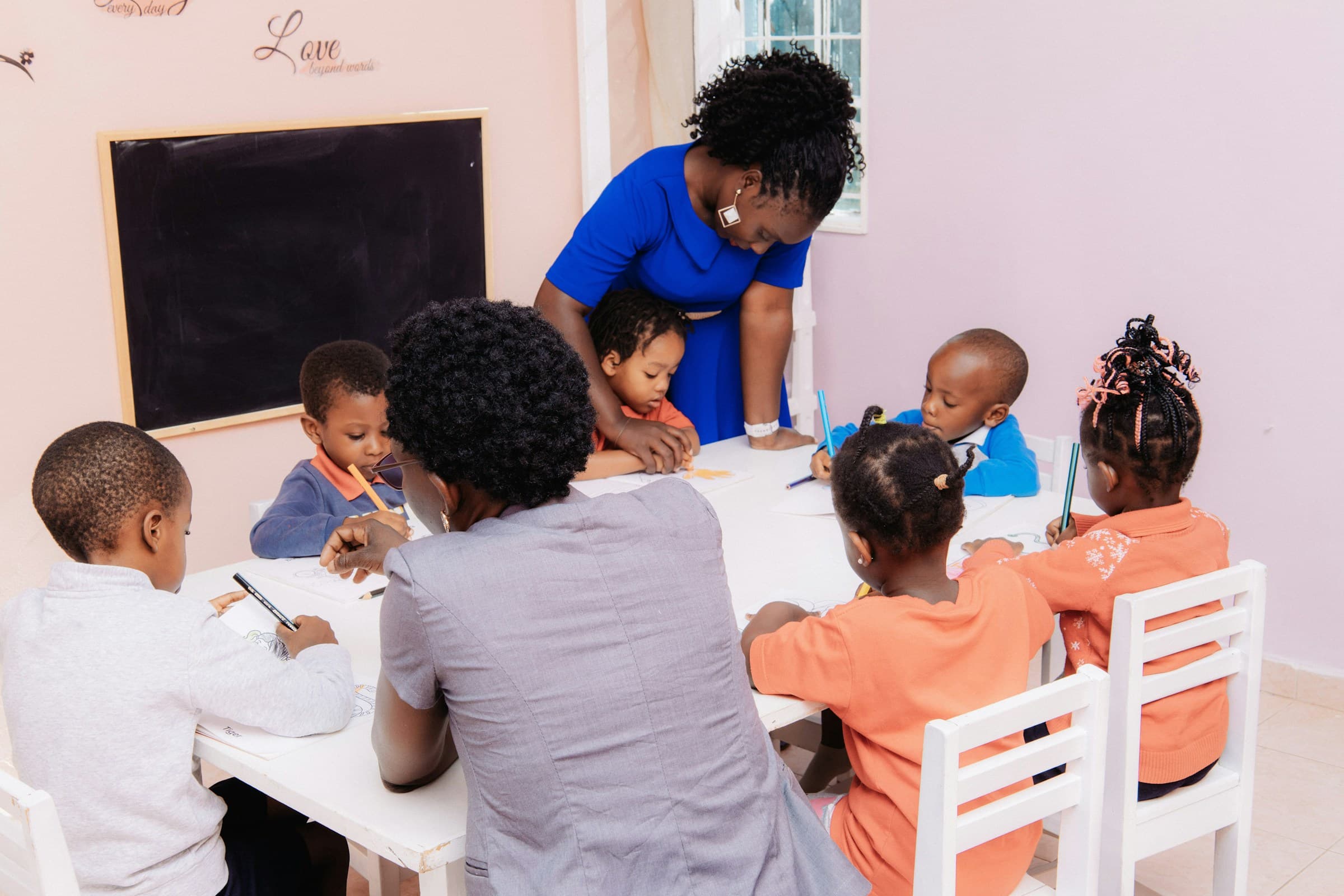 Two educators guiding a small group of young children as they draw and colour at a classroom table